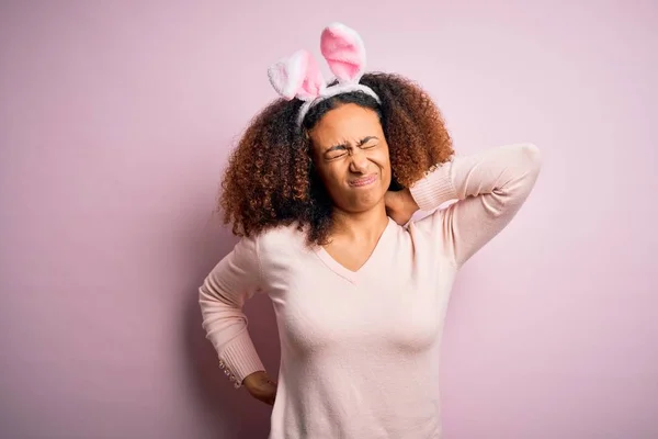 年轻的非洲裔美国女人 头戴非洲式的头发 戴着兔子耳朵 背景粉红 脖子酸痛 手摸脖子 肌肉疼痛 — 图库照片
