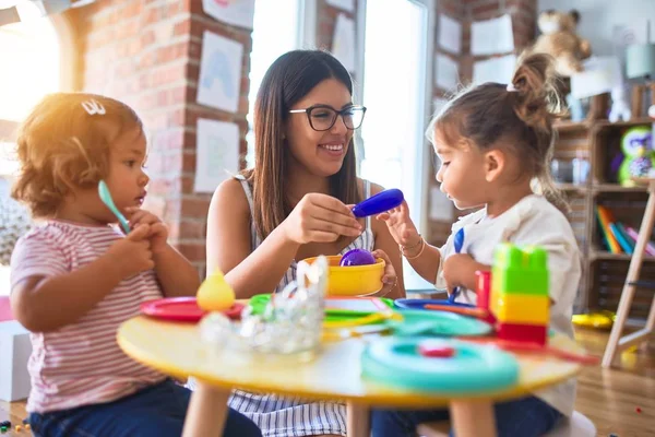 幼稚園でプラスチック製の食べ物やカトラリーのおもちゃを使って食事をする若い美しい先生と幼児 — ストック写真