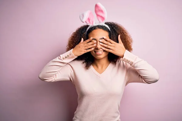 年轻的非洲裔美国女人 有着一头黑发 红红的背景上戴着小兔子耳朵 双手捂住眼睛 笑容满面 笑逐颜开 盲目概念 — 图库照片