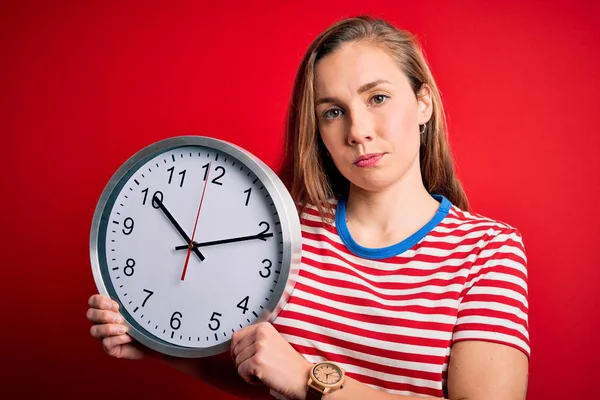 Young Beautiful Blonde Woman Holding Big Clock Standing Isolated Red — Stockfoto