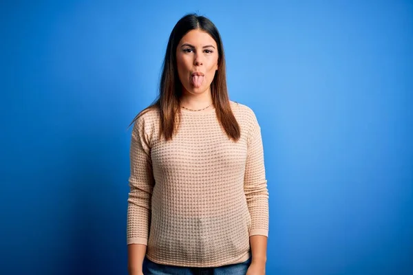 青い背景にカジュアルなセーターを着た若い美しい女性が面白い表情で幸せ舌を突き出しています 感情概念 — ストック写真