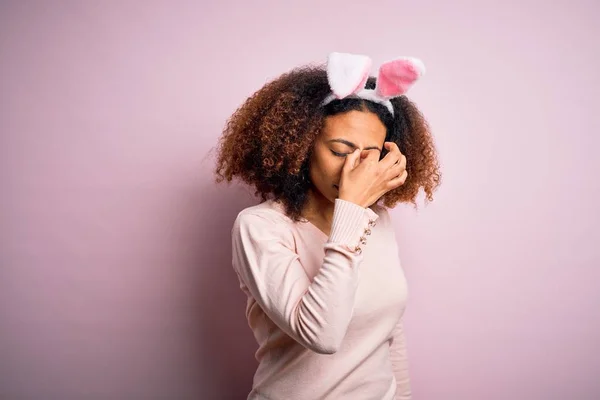 年轻的非洲裔美国女人 头戴黑发 双耳覆盖粉红的背景 疲倦地揉揉鼻子和眼睛 感觉疲劳和头痛 压力和挫败感概念 — 图库照片