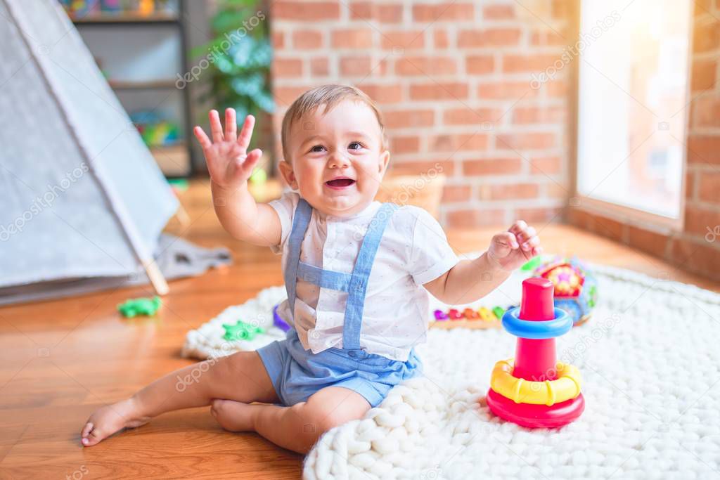 Beautiful toddler sitting on the blanket smiling with hands raised at kindergarten