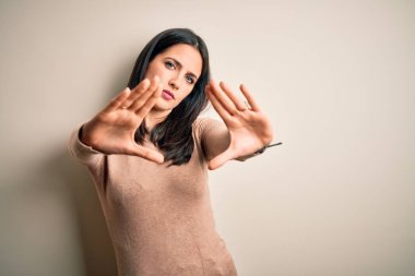 Young brunette woman with blue eyes wearing casual sweater over isolated white background doing frame using hands palms and fingers, camera perspective