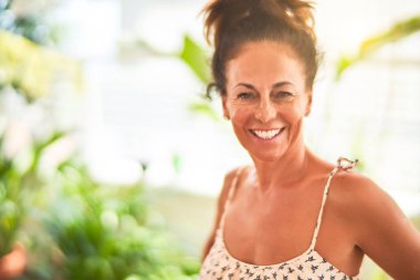 Orta yaşlı güzel bir kadın terasta dikiliyor ve bitkiler gülümsüyor.