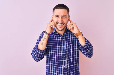 Genç yakışıklı adam izole edilmiş arka planda duruyor. Yüksek sesli müziğin gürültüsü için parmaklarıyla kulakları kapatıyor. Sağır kavramı.