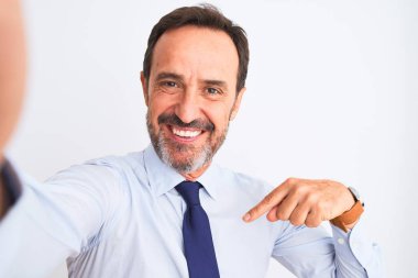 Middle age businessman wearing tie make selfie standing over isolated white background with surprise face pointing finger to himself