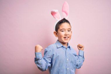 Paskalya tavşanı kulakları takan küçük bir çocuk pembe arka plan üzerinde şaşırmış ve şaşırmış bir şekilde kolları açık ve gözleri açık bir şekilde başarıyı kutluyor. Kazanan konsept.