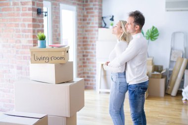 Genç güzel çift yan bakarak karton kutular etrafında yeni evde ayakta, kendine güvenen gülümseme ile doğal yüzü ile profil poz dinlenmek.