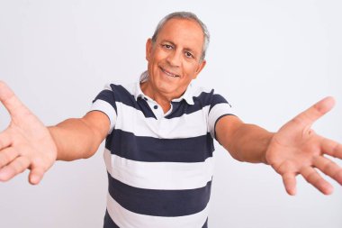 Üstün gri saçlı, sıradan çizgili polo giyen, izole edilmiş beyaz arka planda duran ve sarılmak için kollarını açıp gülümseyen kameraya bakan adam. Mutluluğu kucaklayan neşeli bir ifade..