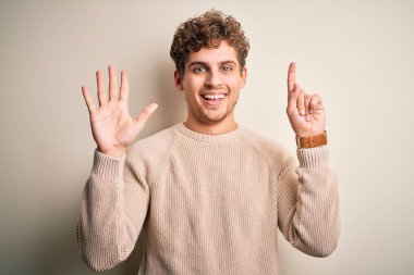 Sarışın, kıvırcık saçlı, beyaz arka planda sıradan bir süveter giyen ve altı numaralı parmaklarını göstererek gülümseyen, kendinden emin ve mutlu genç bir adam..