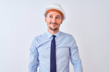 Müteahhit kaskı takan genç bir iş adamı izole edilmiş arka planda gülümsüyor ve diğer tarafa bakıp düşünüyor..