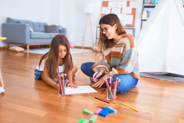 Anaokulundaki bir sürü oyuncağın etrafında kalem ve kağıt kullanarak güzel bir öğretmen ve bebek resmi çiziyor.