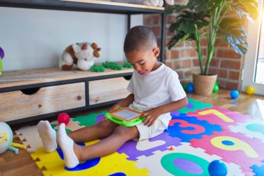 Sevimli Afro-Amerikan bebek yerde oturmuş, anaokulundaki oyuncakların etrafında dijital tahta kullanarak resim çiziyor.