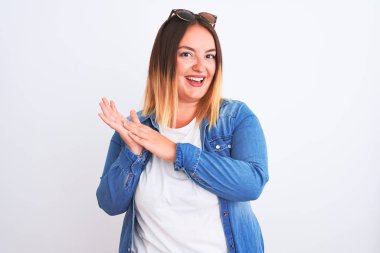 Güzel bir kadın kot gömlek giyiyor, beyaz arka planda duruyor, alkışlıyor ve mutlu ve neşeli, gururlu elleri bir arada alkışlıyor.