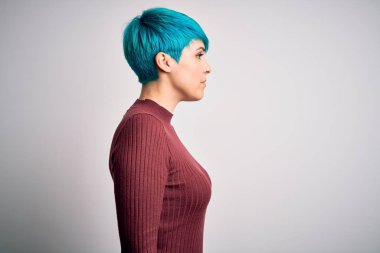 Young beautiful woman with blue fashion hair wearing casual sweater over white background looking to side, relax profile pose with natural face with confident smile.