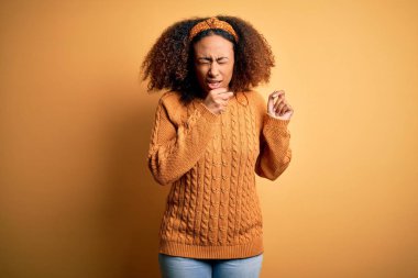 Afro saçlı, sarı arka planda günlük süveter giyen, kendini kötü hisseden ve soğuk algınlığı veya bronşitin belirtisi olarak öksüren Afro Amerikalı genç bir kadın. Sağlık hizmeti kavramı.