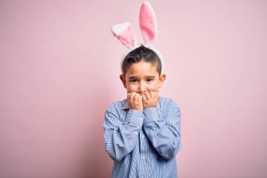 Paskalya tavşanı kulakları takan küçük bir çocuk pembe arka planda gergin ve gergin görünüyor. Endişe sorunu.