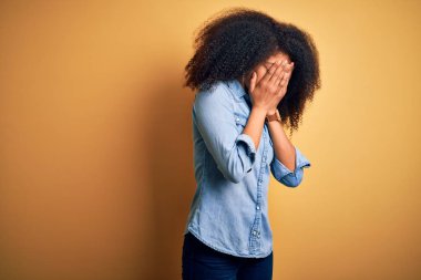 Young beautiful african american woman with afro hair standing over yellow isolated background with sad expression covering face with hands while crying. Depression concept.
