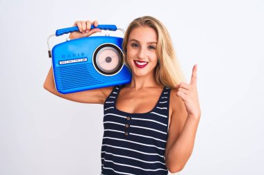 Young beautiful woman holding vintage radio standing over isolated white background surprised with an idea or question pointing finger with happy face, number one