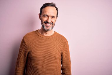 Orta yaşlı, beyaz, günlük kahverengi süveter giyen, mutlu ve havalı bir gülümsemeyle izole edilmiş pembe arka planda duran bir adam. Şanslı kişi..