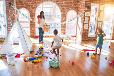 Anaokulunda bir sürü oyuncağın etrafında basketbol oynayan genç ve güzel öğretmenler ve yeni yürümeye başlayan çocuklar.