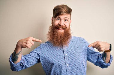 Handsome Irish redhead business man with beard standing over isolated background looking confident with smile on face, pointing oneself with fingers proud and happy.