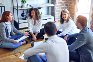 Bir grup iş adamı mutlu ve kendinden emin gülümsüyor. Yerde oturup rahatlamak birlikte çalışmak, konuşmak ve ofiste belgeleri okumak.