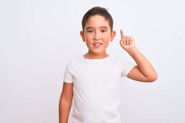 İzole edilmiş beyaz arka plan üzerinde duran ve gülümseyen, kendinden emin ve mutlu gülümseyen güzel çocuk tişörtü giyiyor..