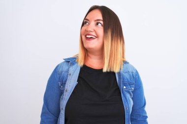 İzole edilmiş beyaz arka plan üzerinde duran kot gömlek giyen genç ve güzel bir kadın yüzünde gülümseme, doğal bir ifade ile bir o yana bir bu yana bakıyor. Kendinden emin gülen.