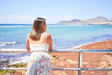 Güzel genç bir kadın kumsalda yürüyor okyanus manzarasının tadını çıkarıyor yaz tatilinde gülümsüyor.