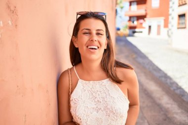 Turuncu duvara yaslanan güzel kız, güneşli bir yaz gününde gülümseyen genç arkadaş.