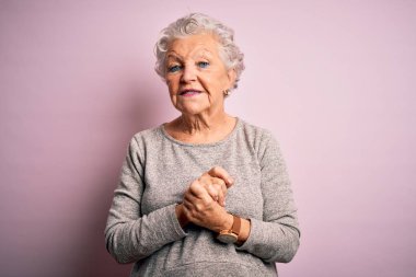 Son sınıf güzeli, rahat tişört giyen, pembe arka planda duran, elleri çapraz parmaklı rahat ve neşeli gülümseyen bir kadın. Başarı ve iyimser