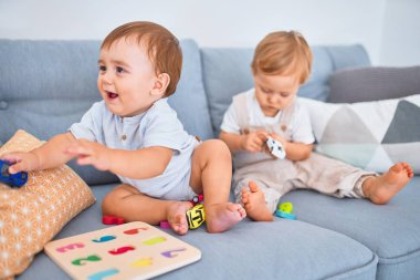 Kanepede oturup evde oyuncaklarla oynayan güzel bebekler.