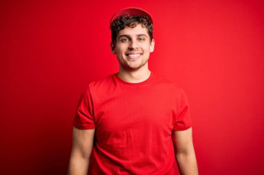 Sarışın, kıvırcık saçlı, soyutlanmış kırmızı arka planda duran mutlu ve havalı bir gülümsemesi olan bir teslimatçı. Şanslı kişi..