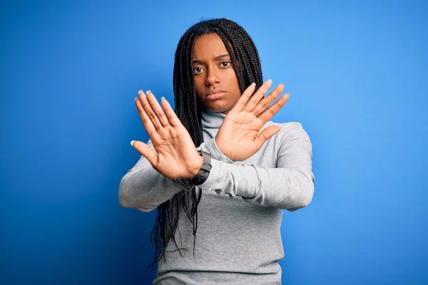 Young african american woman standing wearing casual turtleneck over blue isolated background Rejection expression crossing arms doing negative sign, angry face