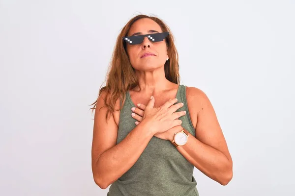 Middle age mature woman wearing thug life sunglasses over isolated background smiling with hands on chest with closed eyes and grateful gesture on face. Health concept.