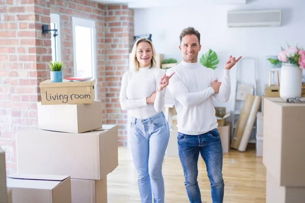 Genç ve güzel bir çift, yeni evlerinde karton kutuların etrafında durmuş, yüzünde kocaman bir gülümsemeyle, elleri ve parmaklarıyla kameraya bakıyor..
