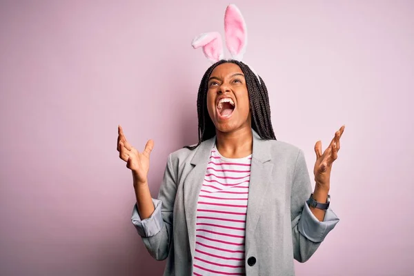 年轻的非洲裔美国女孩 戴着可爱的复活节兔子耳朵 粉红的背景 疯狂的大叫和喊叫 带有攻击性的表情和手臂 沮丧的概念 — 图库照片