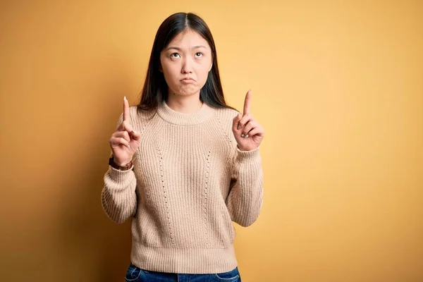 年轻美丽的亚洲女人 穿着休闲装 披着黄色的孤立的背景 带着忧伤和不安的表情 用手指指示方向 不快乐和沮丧 — 图库照片