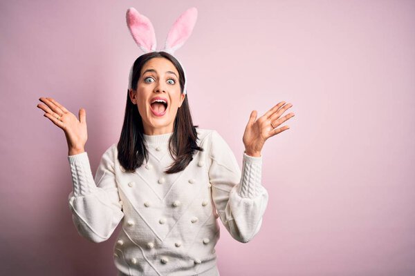Young caucasian woman wearing cute easter rabbit ears over pink isolated background celebrating crazy and amazed for success with arms raised and open eyes screaming excited. Winner concept