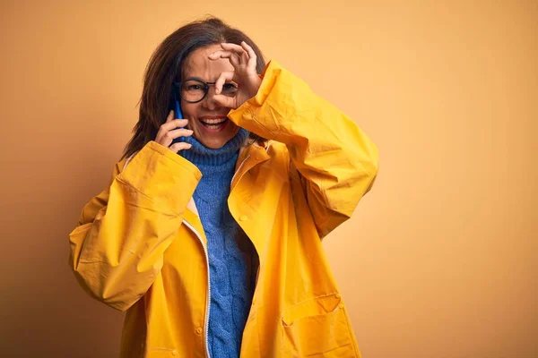 中世の女性を身に着けています黄色のレインコートの呼び出しを使用してスマートフォン幸せな顔笑顔をします — ストック写真