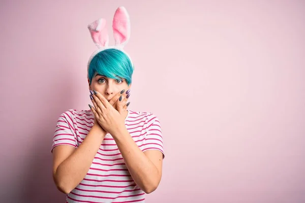 一位年轻的女人 留着时髦的蓝色头发 带着粉色背景的东亚兔耳朵 双手捂住嘴 为自己的错误感到震惊 秘密概念 — 图库照片