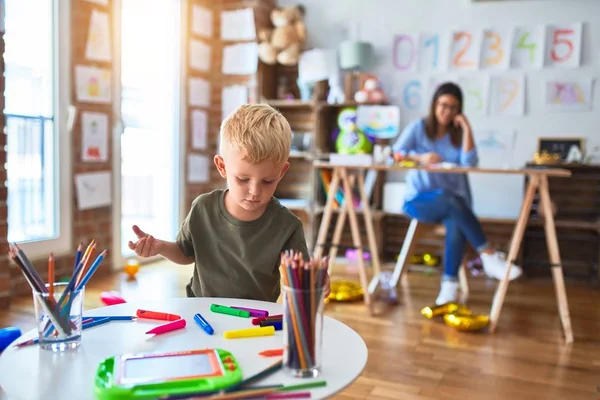 若い白人の子供は教師と一緒に学校で遊んでいる 母と息子は遊び場で色鉛筆で絵を描く若い女性は机の上に座っている — ストック写真