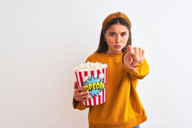 İzole edilmiş beyaz arka planda duran patlamış mısır paketini tutan genç ve güzel bir kadın kamerayı işaret ediyor ve sen, el işareti, ön taraftan pozitif ve kendinden emin bir jest.