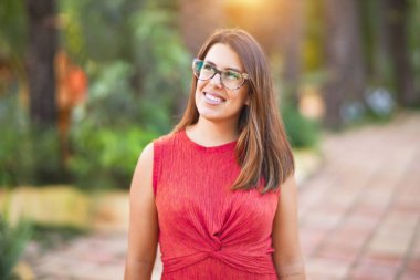 Genç ve güzel bir kız gülümseyerek mutlu ve kendinden emin bir şekilde parkta yürüyor, yüzünde bir gülümsemeyle duruyor.