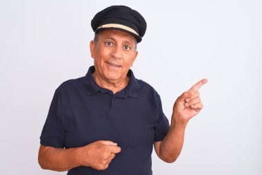 Senior grey-haired man wearing black polo and captain hat over isolated white background with a big smile on face, pointing with hand and finger to the side looking at the camera.