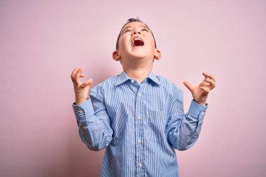 Zarif bir gömlek giyen küçük çocuk pembe izole edilmiş arka plan üzerinde duruyor çılgın ve kızgın bir şekilde bağırıyor ve agresif bir ifade ve kollarla bağırıyor. Hayal kırıklığı konsepti.