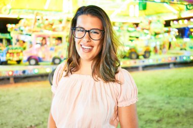 Gözlük takan genç ve güzel bir kadın gecenin ışıklarında mutlu ve heyecanlı bir şekilde gülümsüyor.