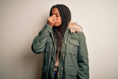 Genç Afro-Amerikalı kadın izole arka planda kışlık parka palto giyiyor. Burun ve gözler sürtünüyor, yorgunluk ve baş ağrısı hissediyor. Stres ve hüsran kavramı.